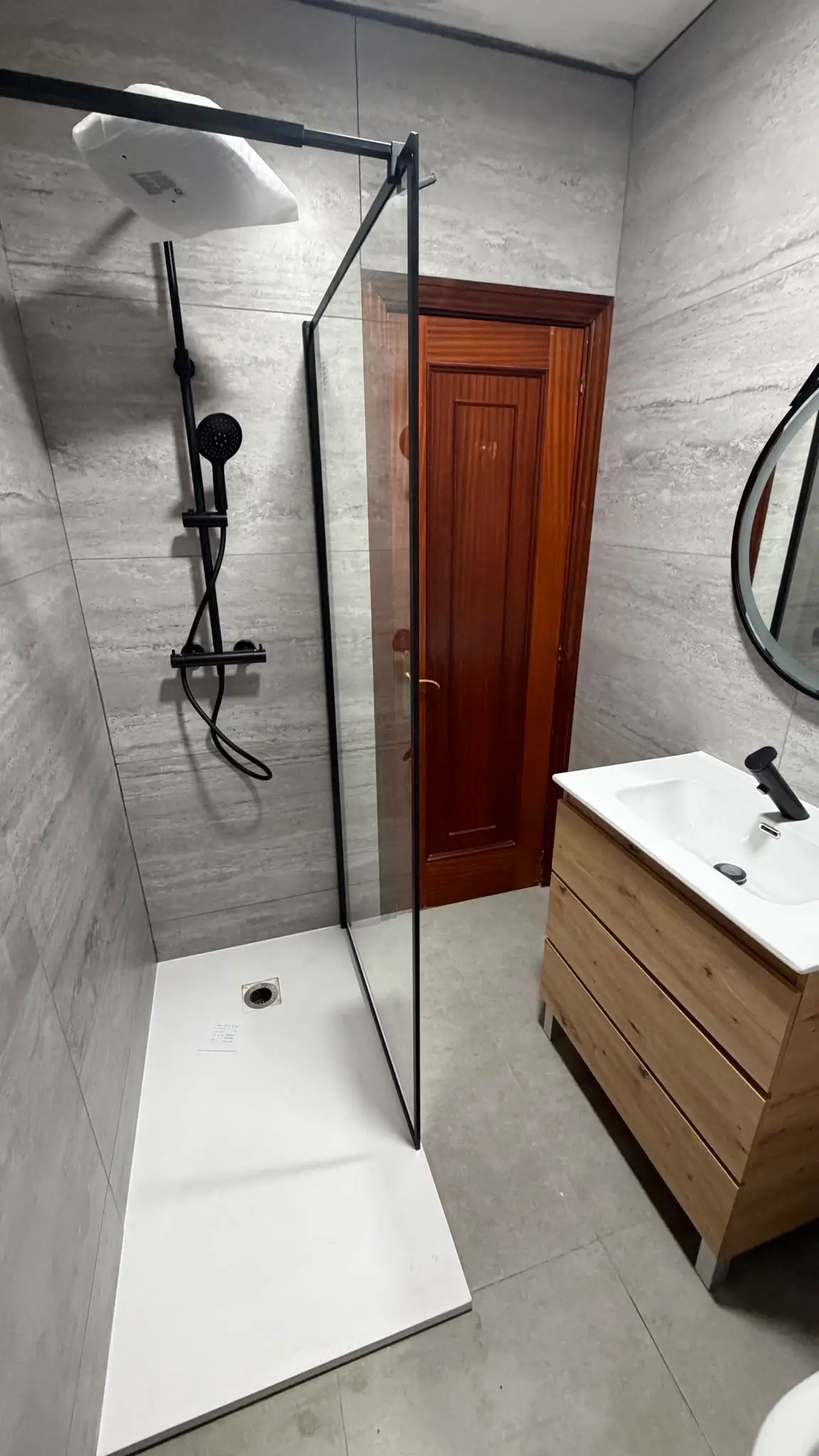 Reforma de baño con mampara de perfilería negra, plato de ducha blanco y mueble de madera en Coruña