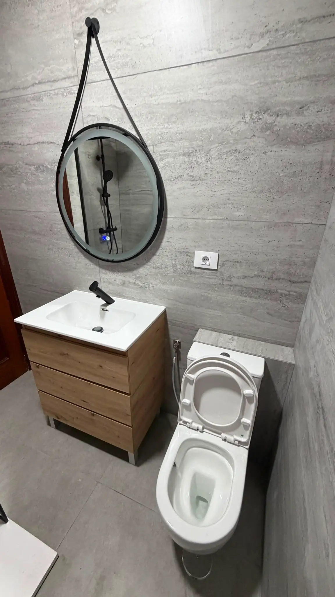 Reforma de baño con mueble de madera, espejo circular retroiluminado y revestimiento gris en Coruña