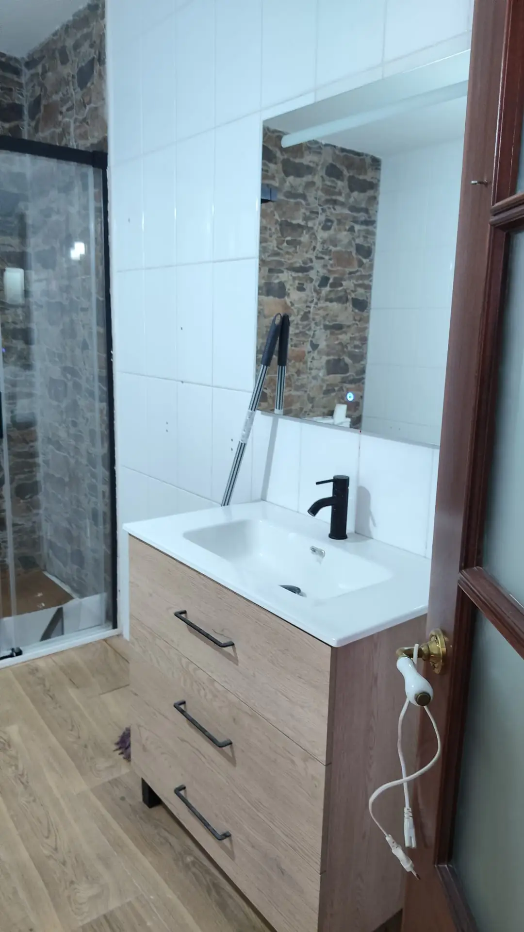 Reforma de baño con mueble de madera, grifería negra y pared de piedra en Coruña