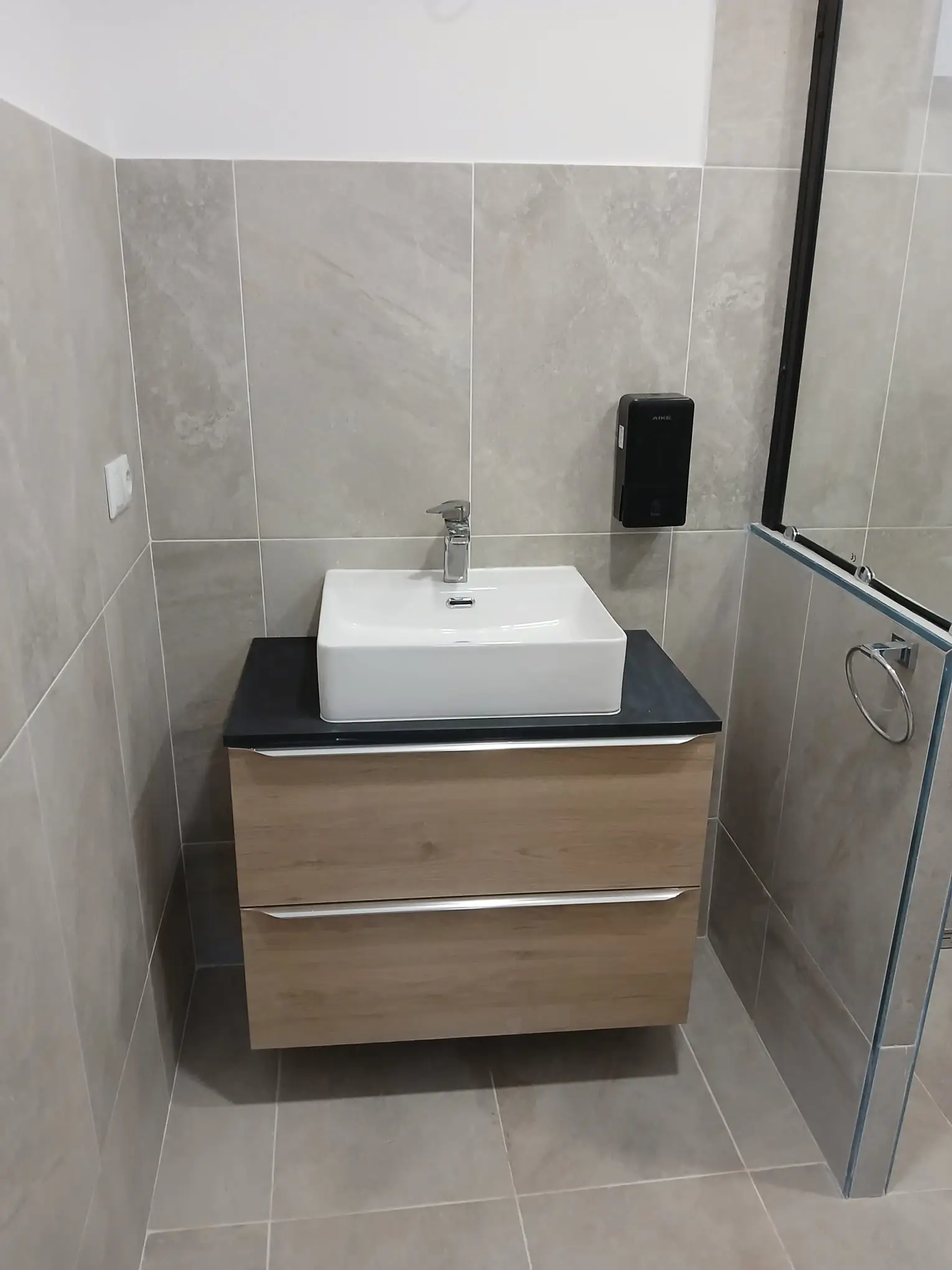 Reforma de baño con mueble suspendido de madera y lavabo sobre encimera negra en A Coruña