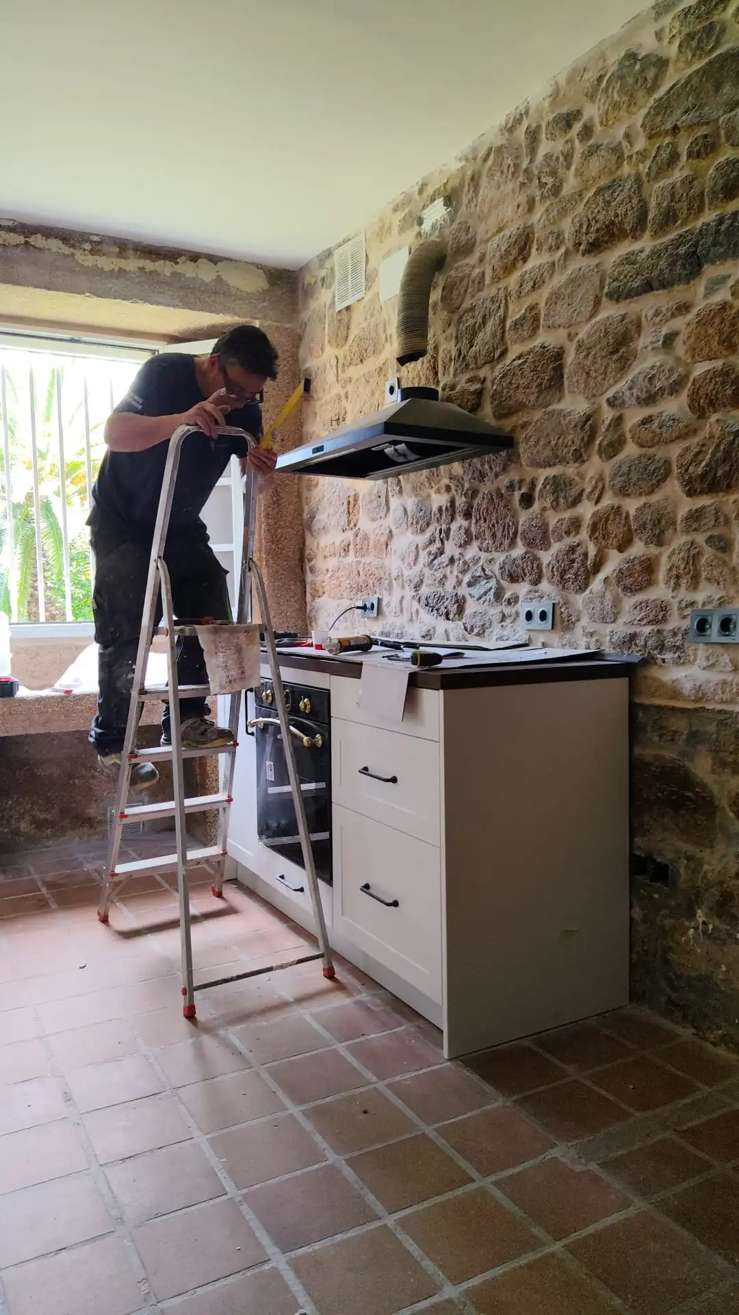 Operario en una reforma de cocina instalando muebles sobre pared de piedra vista en Coruña